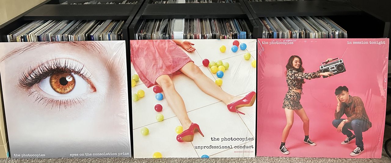 The Photocopies LPs Eyes on the Consolation Prize, Unprofessional Conduct (second edition), and In Session Tonight placed in front of a record collection
